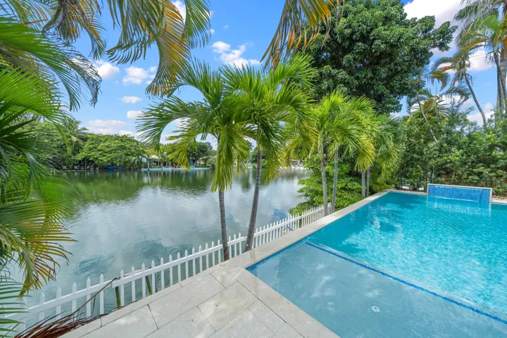 Waterfront property featuring an in-ground swimming pool, white picket fence, and mature palm trees