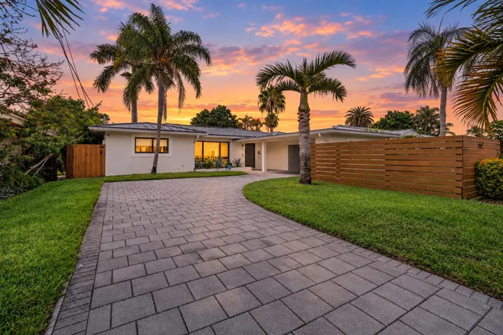 Paved driveway, manicured lawn, horizontal wood fencing, large picture windows, and mature palm trees