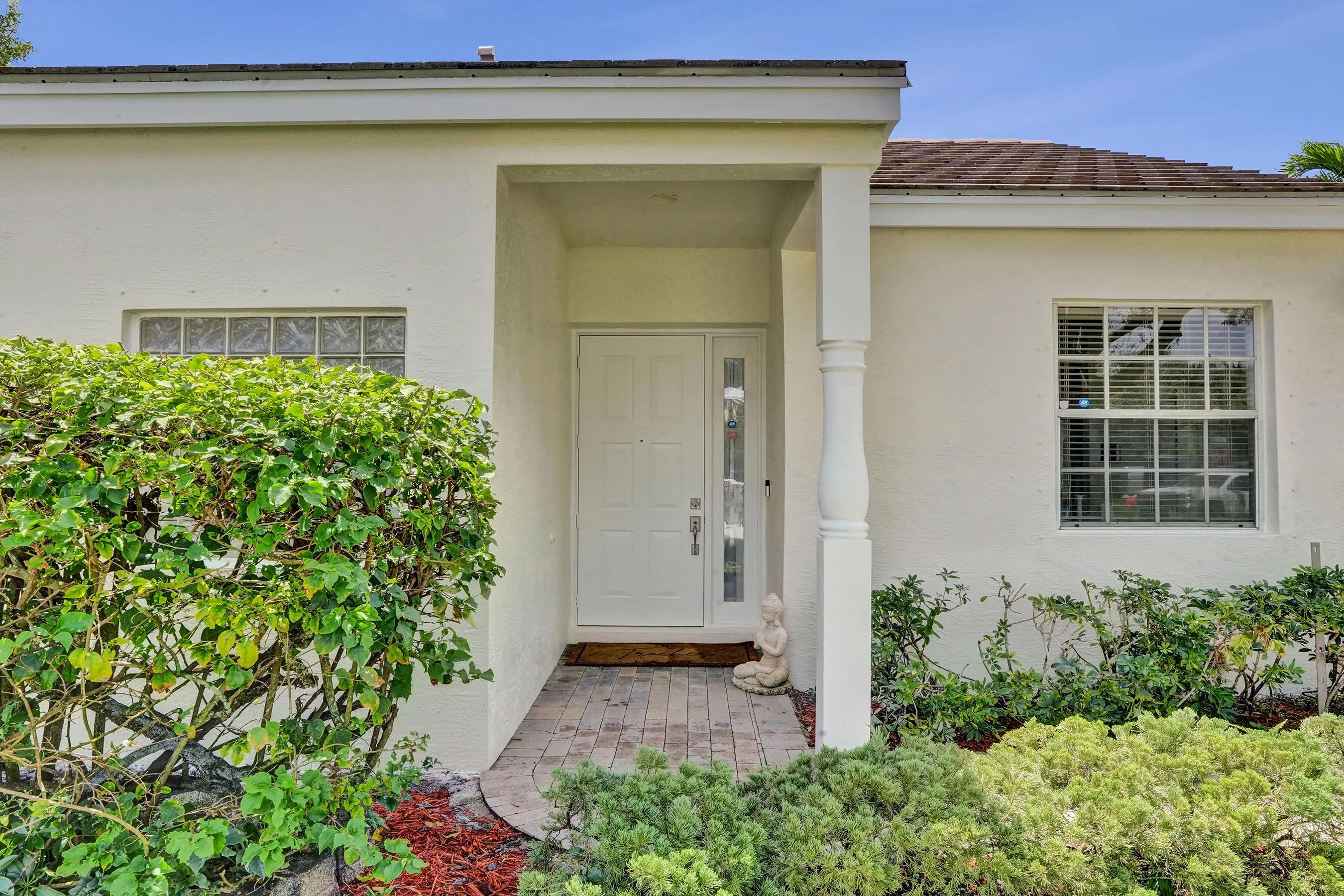 Entryway featuring a white paneled door with decorative glass inserts, a brick paver walkway, and a covered porch supported by a decorative column
