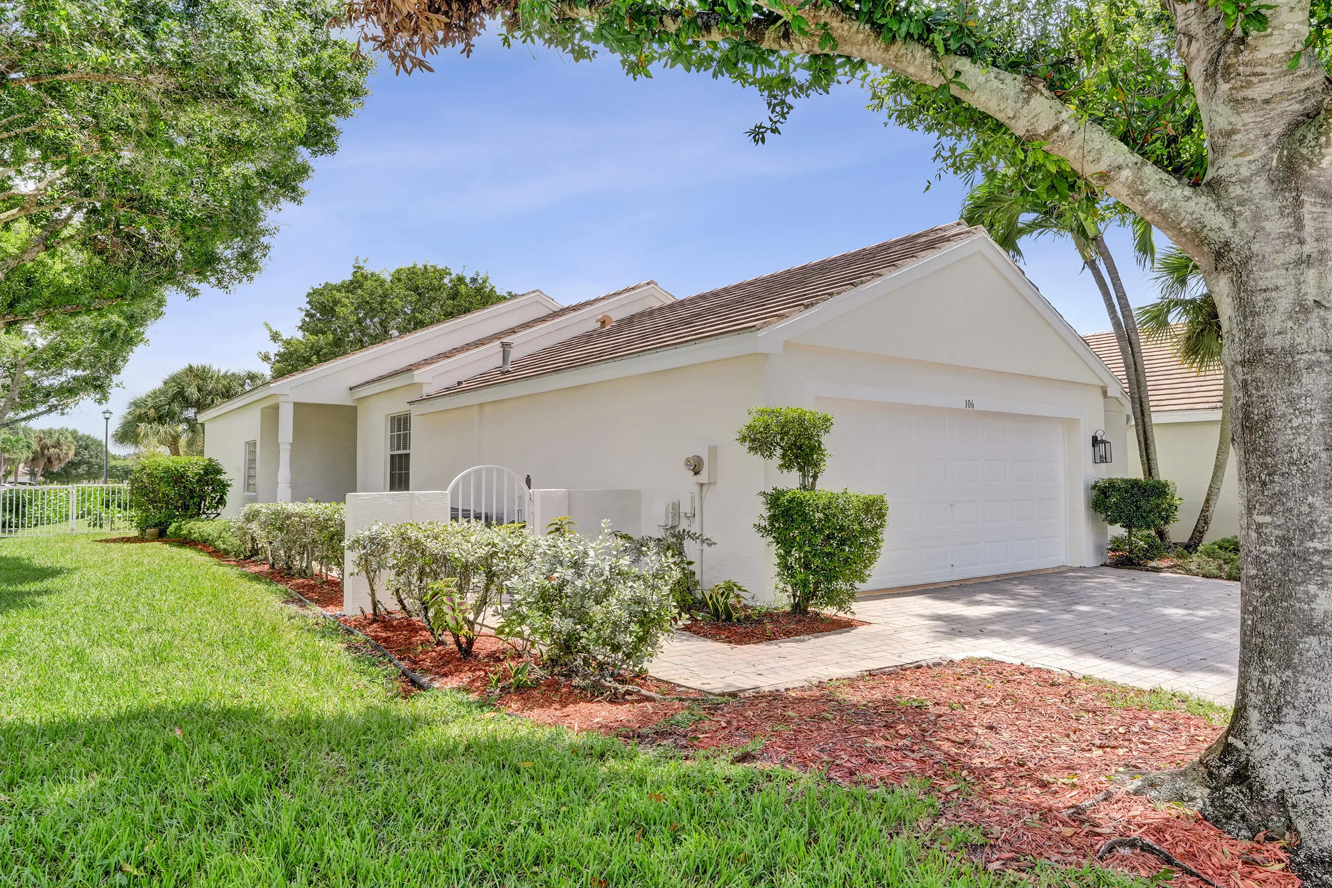 White stucco exterior with a brown tile roof, integrated garage, and a paver driveway