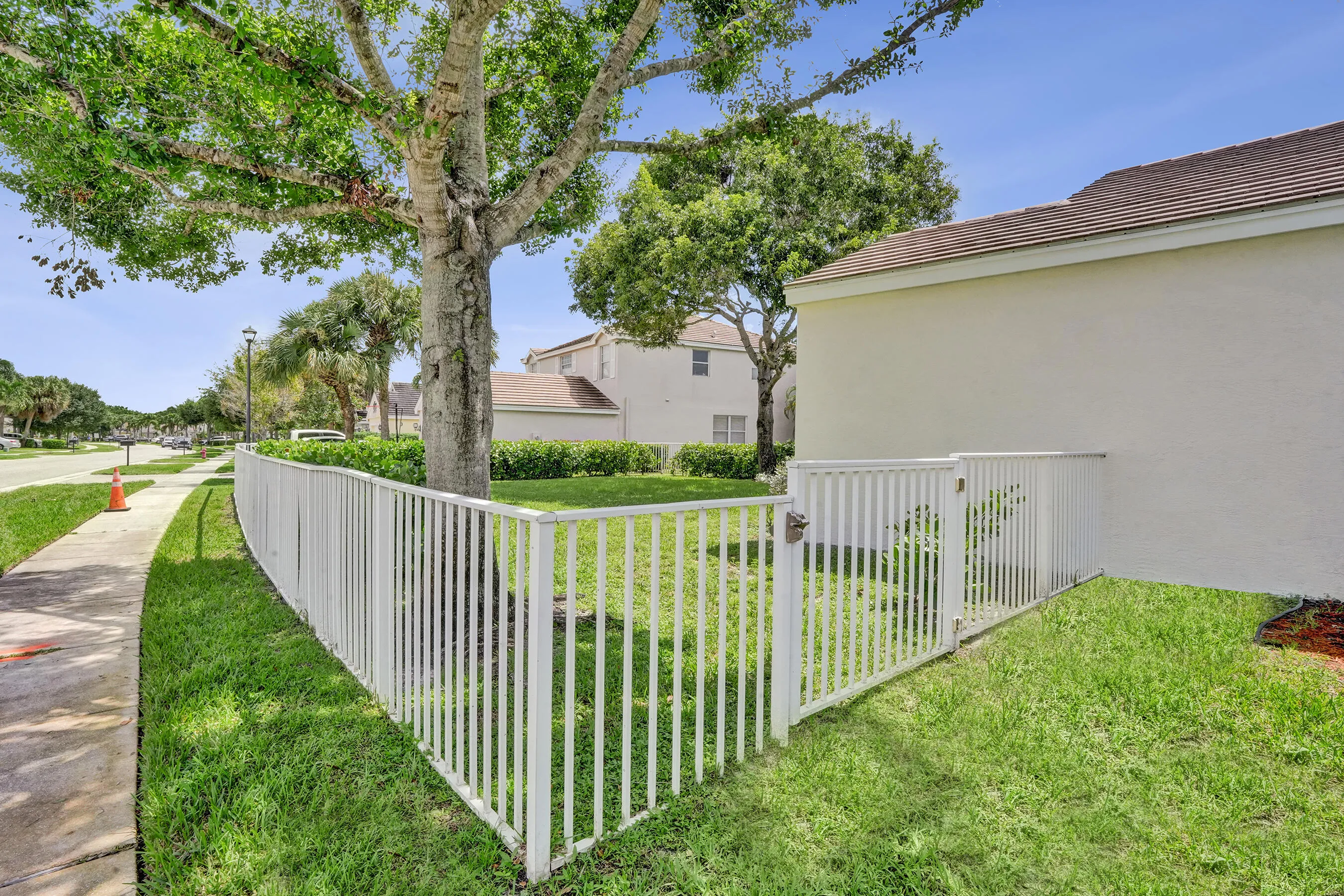 White picket fence with gated access, mature trees, and a paved sidewalk