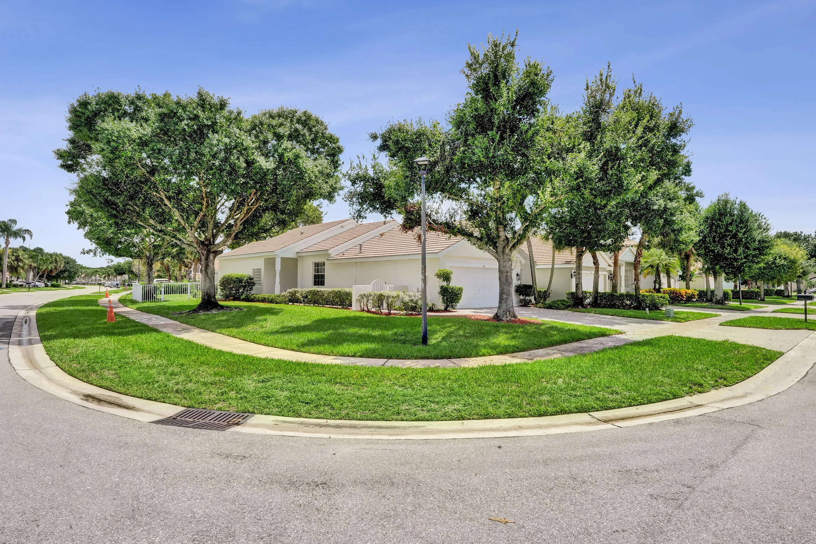 Corner lot residence featuring a white exterior, attached two-car garage, mature trees, and a concrete sidewalk