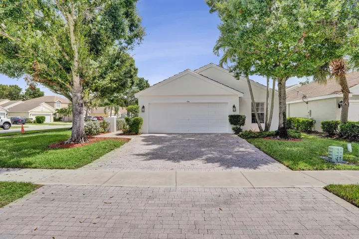 Single-story residence featuring a white exterior, attached garage, and a paver driveway