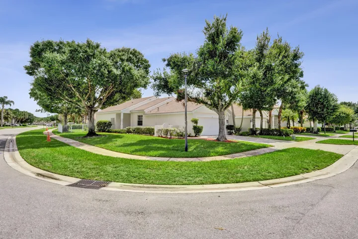 Corner lot residence featuring a white exterior, attached two-car garage, mature trees, and a concrete sidewalk