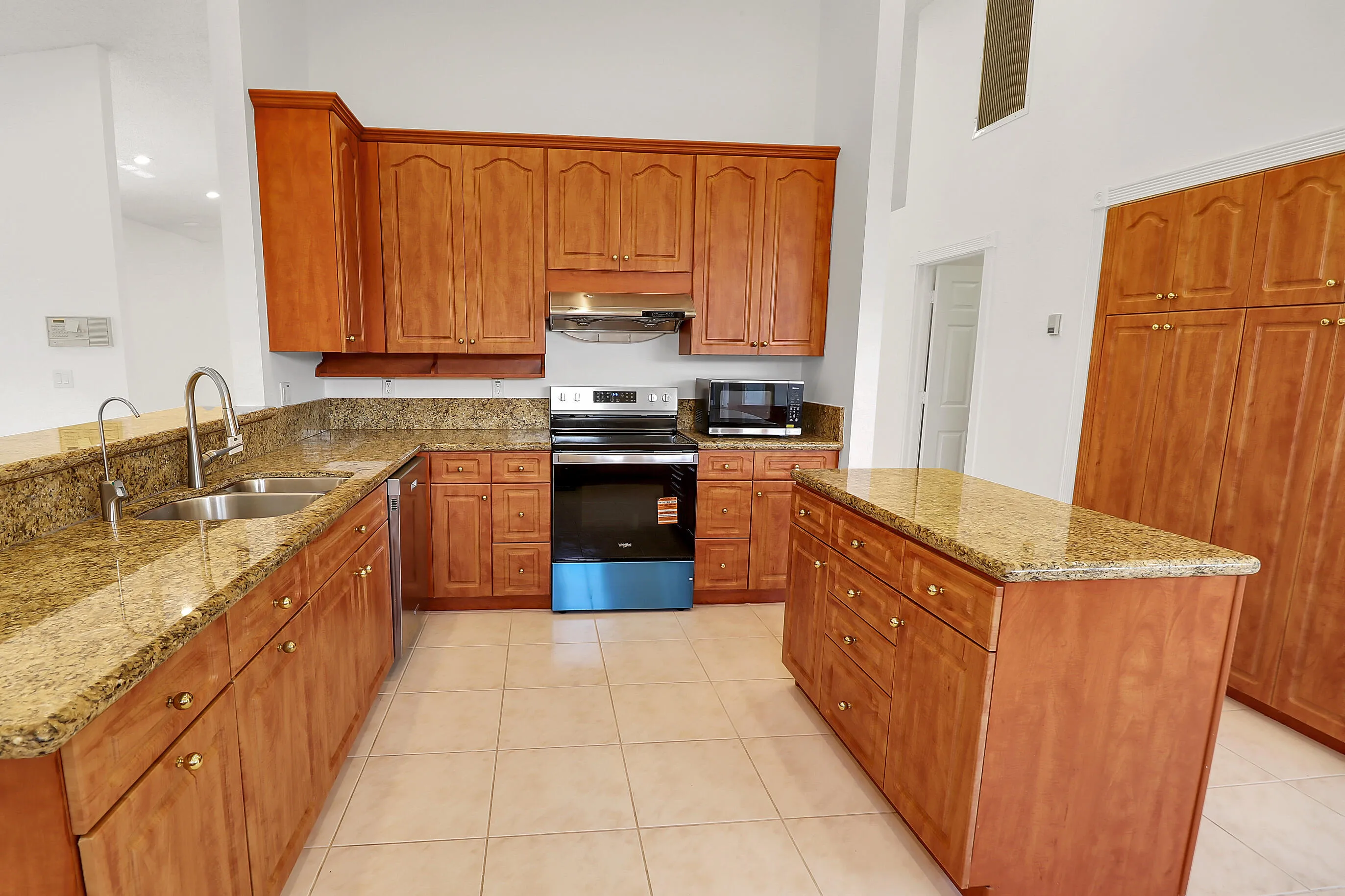 Kitchen featuring extensive wood cabinetry, granite countertops, a central island, stainless steel appliances, and tiled flooring