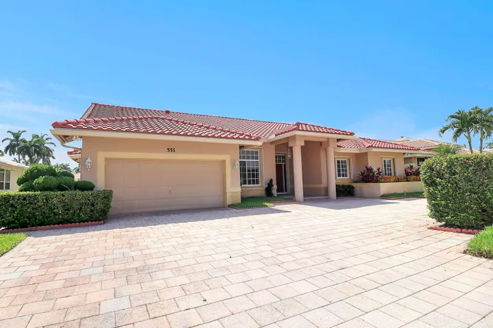 Mediterranean-style exterior featuring a clay tile roof, stucco finish, paver driveway, two-car garage, and established landscaping