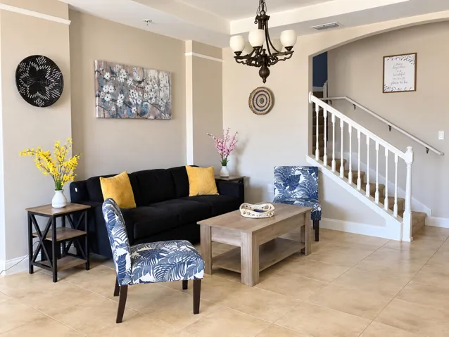 Furnished living room with tile flooring and staircase access.