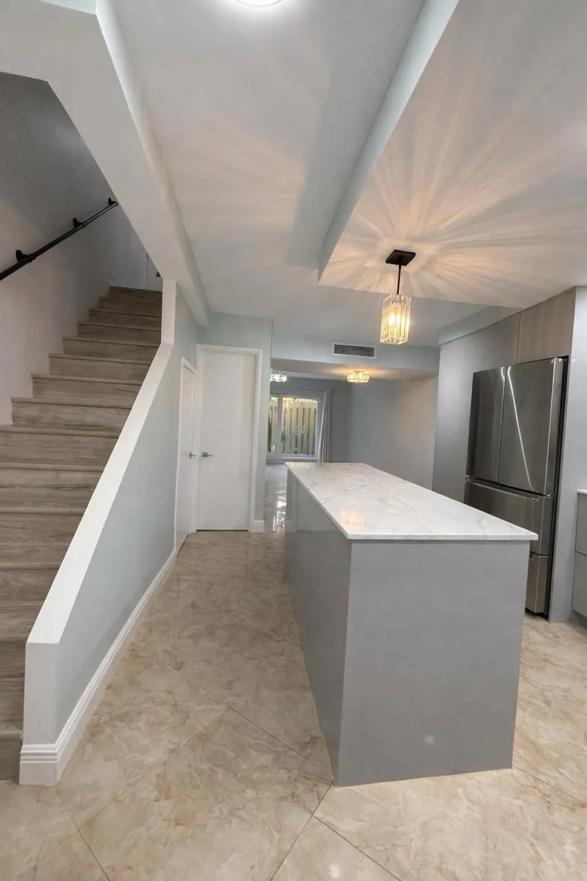 Contemporary kitchen island with a stone countertop, stainless steel refrigerator, recessed lighting, and tile flooring