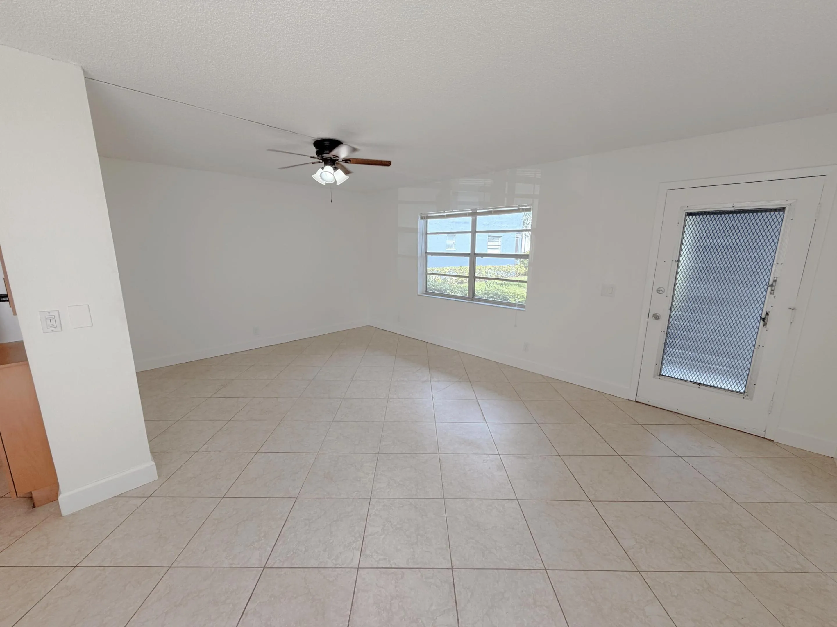 Spacious room featuring neutral-toned tile flooring, a window with exterior visibility, a ceiling fan with integrated lighting.