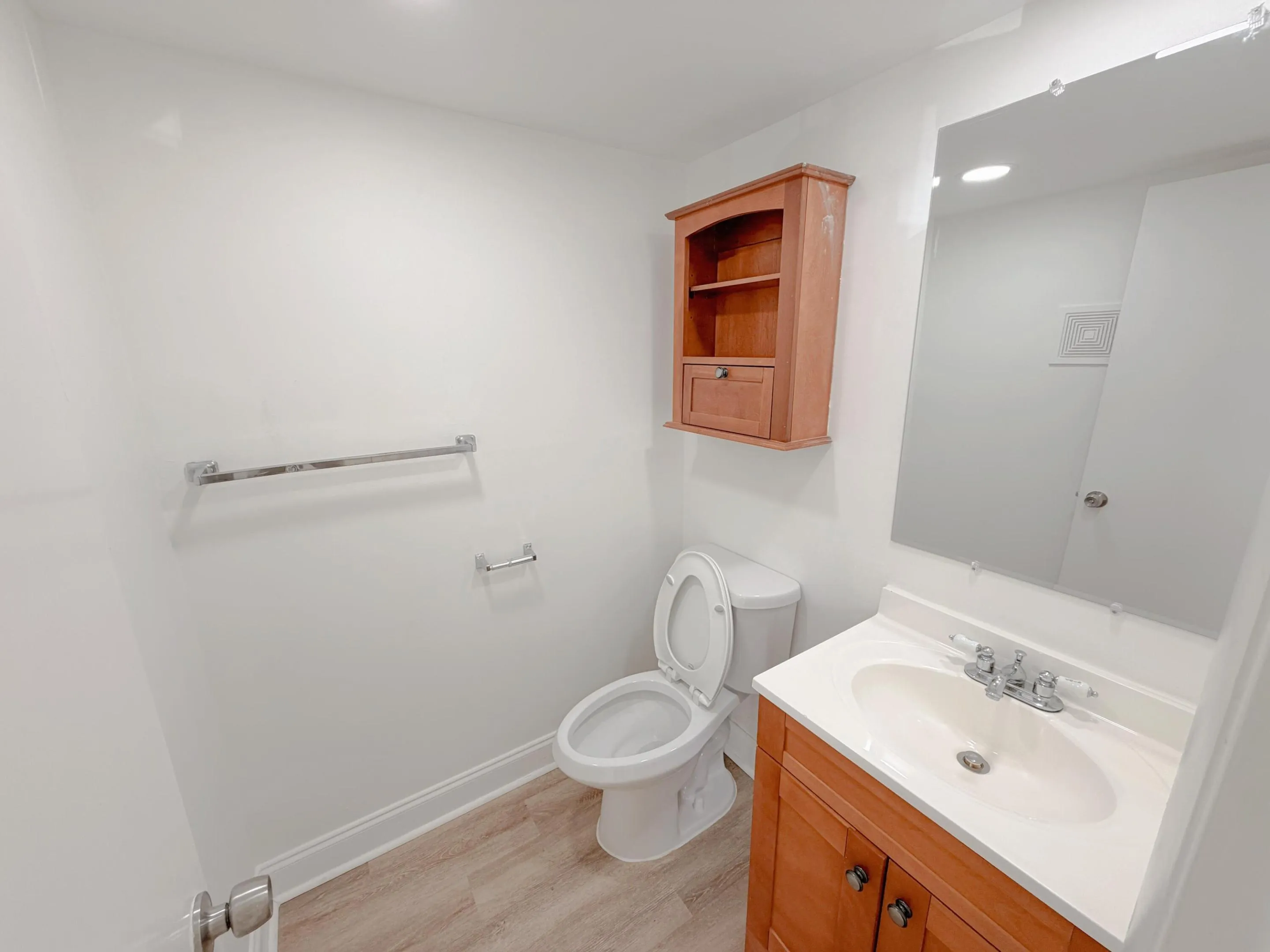 Clean and functional bathroom featuring a wood-finish vanity with integrated sink, white ceramic toilet, and large mirror with integrated lighting