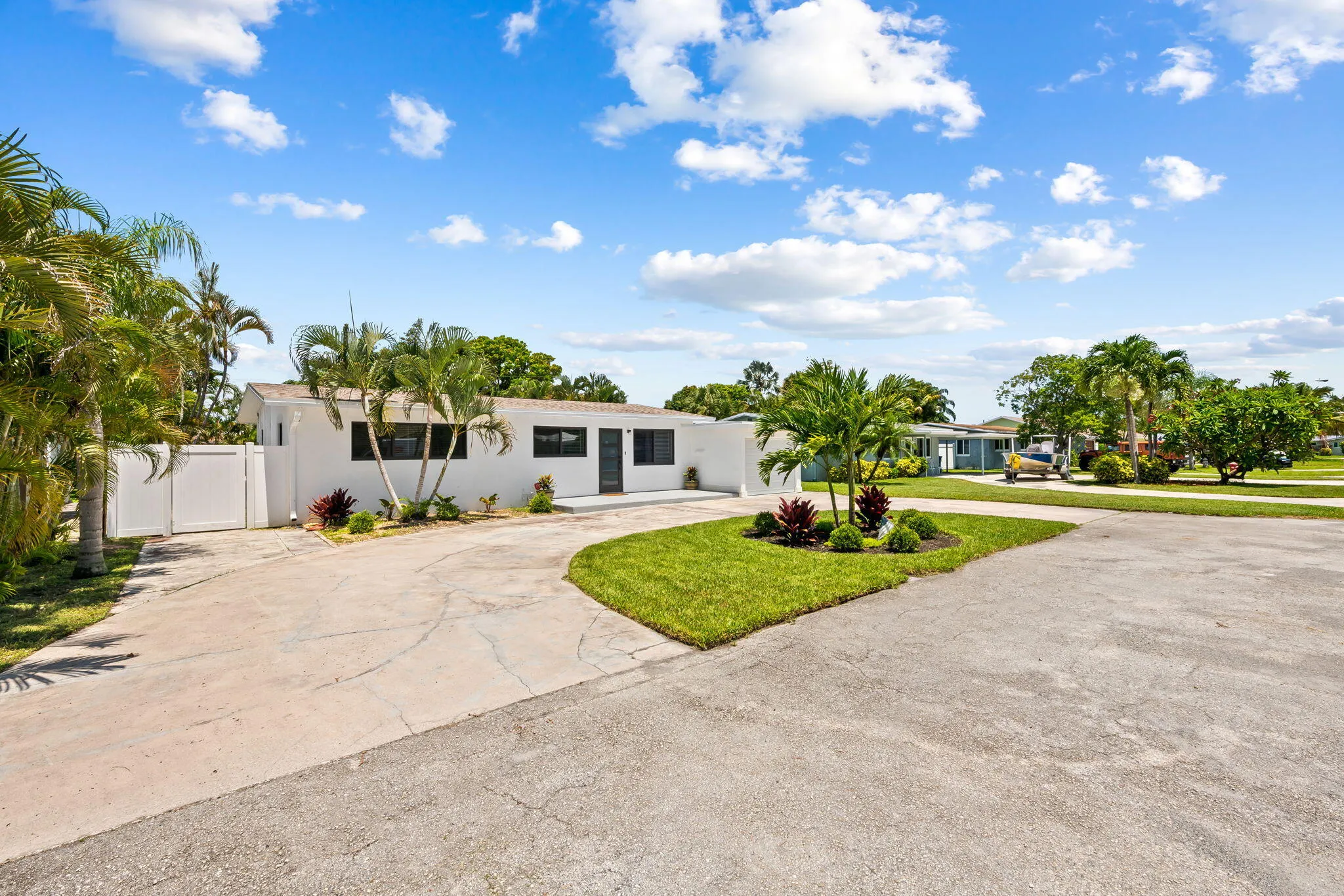White exterior with black-framed windows, surrounded by mature palm trees and landscaped planting beds