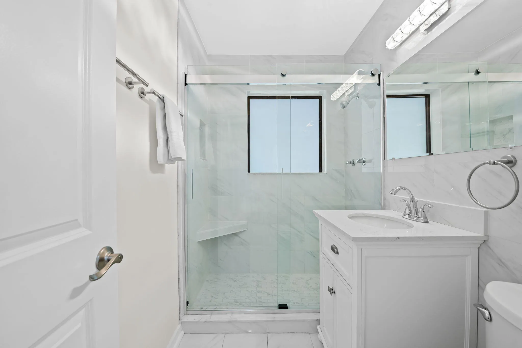 Glass-enclosed shower with a built-in bench, a white vanity with an integrated sink, and chrome fixtures