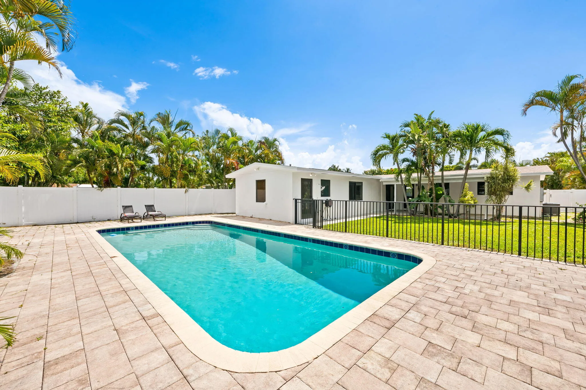 Rectangular swimming pool with paver decking, enclosed by a black metal fence, and surrounded by a white privacy fence