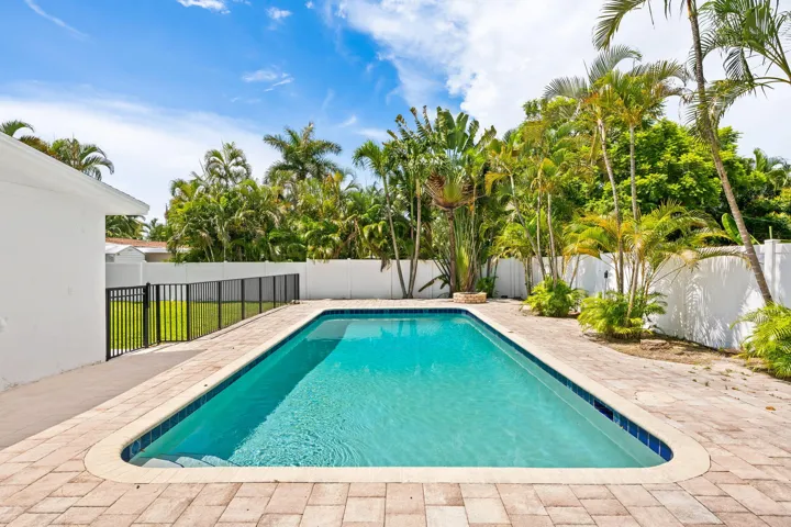 Rectangular swimming pool with curved corners, paver decking, and a black metal fence enclosing a grass area