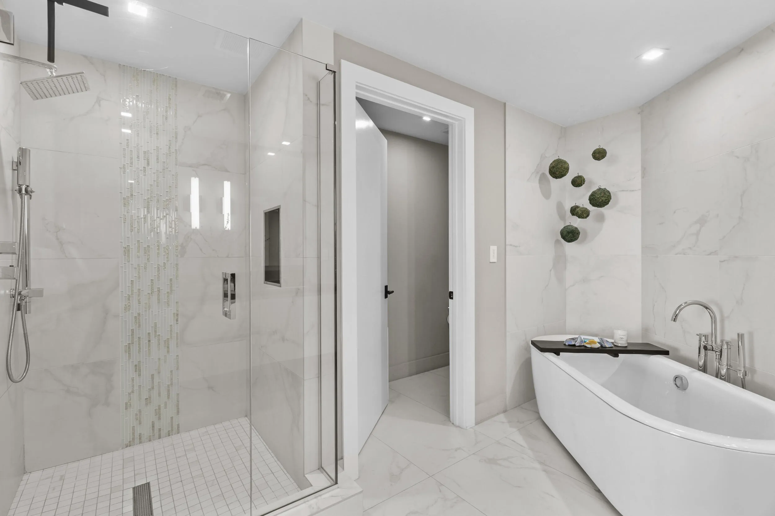 A private spa within the primary suite, this exquisite bathroom showcases custom porcelain tile, a frameless glass shower, a freestanding soaking tub and a floating vanity topped with leathered quartzite, all beautifully illuminated by custom designer sconces.