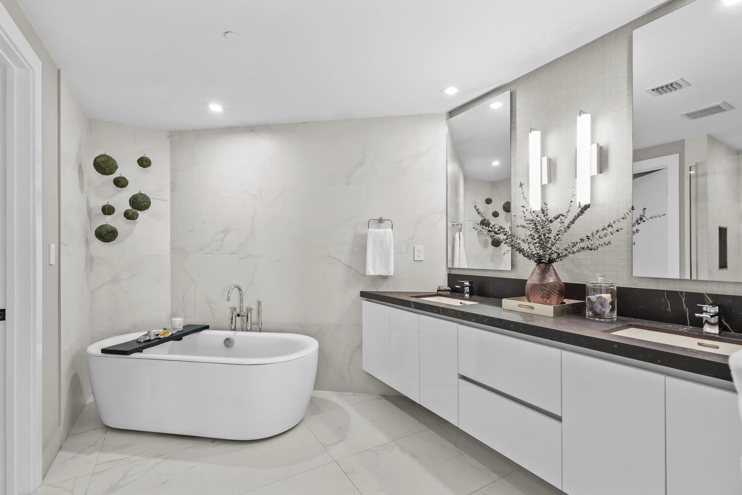 A private spa within the primary suite, this exquisite bathroom showcases custom porcelain tile, a frameless glass shower, a freestanding soaking tub and a floating vanity topped with leathered quartzite, all beautifully illuminated by custom designer sconces.