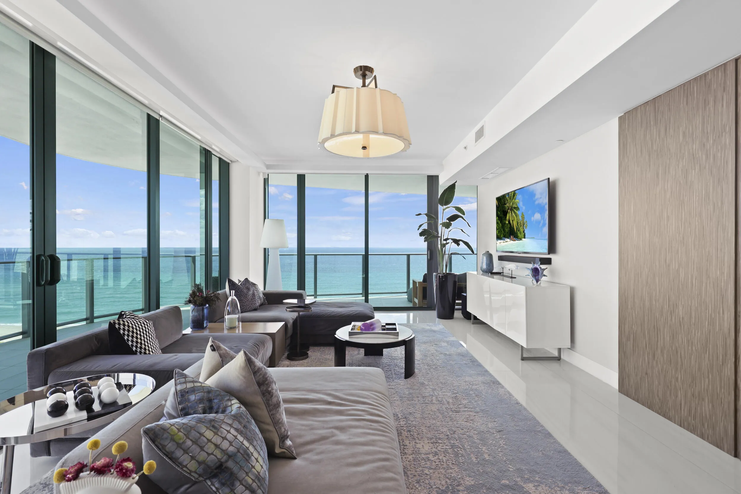 Framed by floor-to-ceiling impact glass, the living room opens seamlessly onto the wraparound balcony, creating an inviting retreat to unwind while enjoying sweeping views and refreshing ocean breezes.