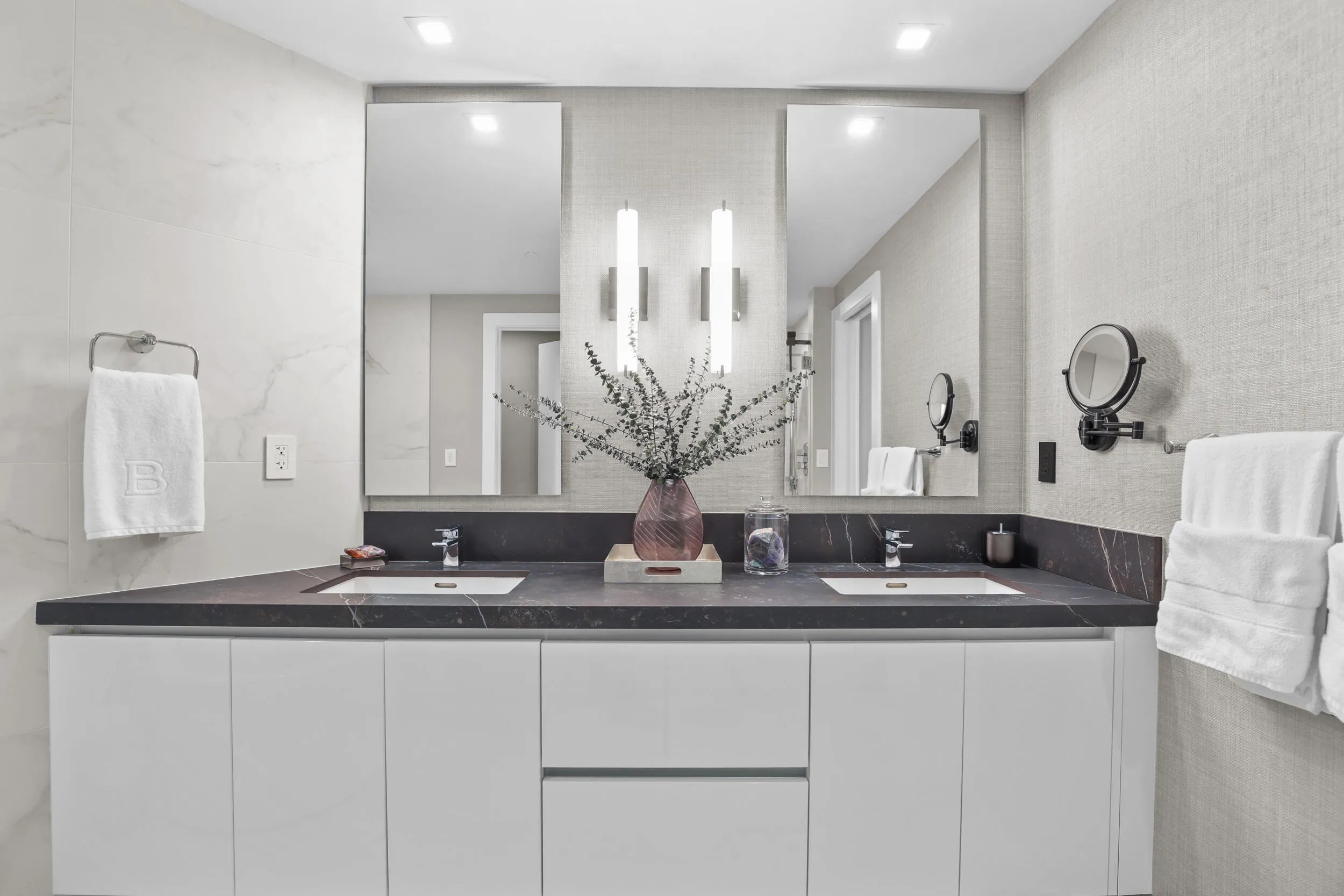 A private spa within the primary suite, this exquisite bathroom showcases custom porcelain tile, a frameless glass shower, a freestanding soaking tub and a floating vanity topped with leathered quartzite, all beautifully illuminated by custom designer sconces.