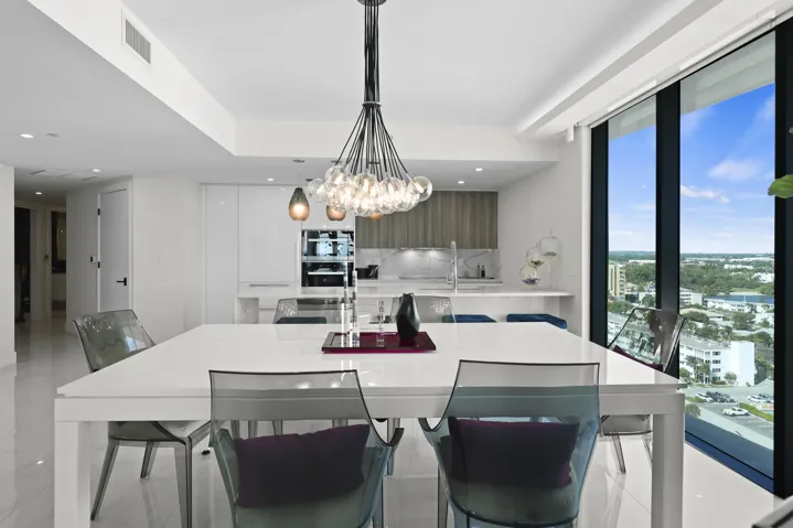The dining area is illuminated by a designer chandelier and custom accent lighting, all framed by captivating views of the Atlantic Ocean and Intracoastal Waterway.