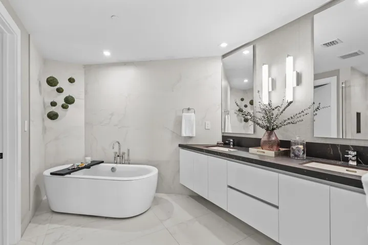 A private spa within the primary suite, this exquisite bathroom showcases custom porcelain tile, a frameless glass shower, a freestanding soaking tub and a floating vanity topped with leathered quartzite, all beautifully illuminated by custom designer sconces.