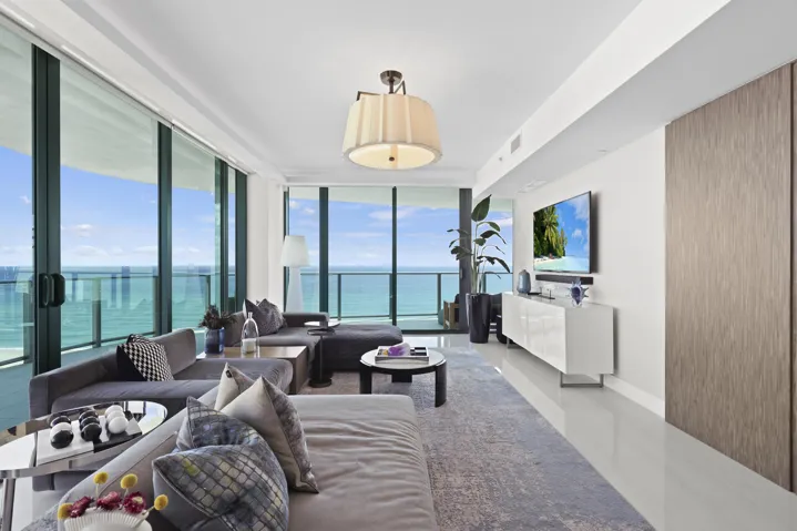 Framed by floor-to-ceiling impact glass, the living room opens seamlessly onto the wraparound balcony, creating an inviting retreat to unwind while enjoying sweeping views and refreshing ocean breezes.