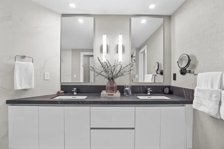 A private spa within the primary suite, this exquisite bathroom showcases custom porcelain tile, a frameless glass shower, a freestanding soaking tub and a floating vanity topped with leathered quartzite, all beautifully illuminated by custom designer sconces.