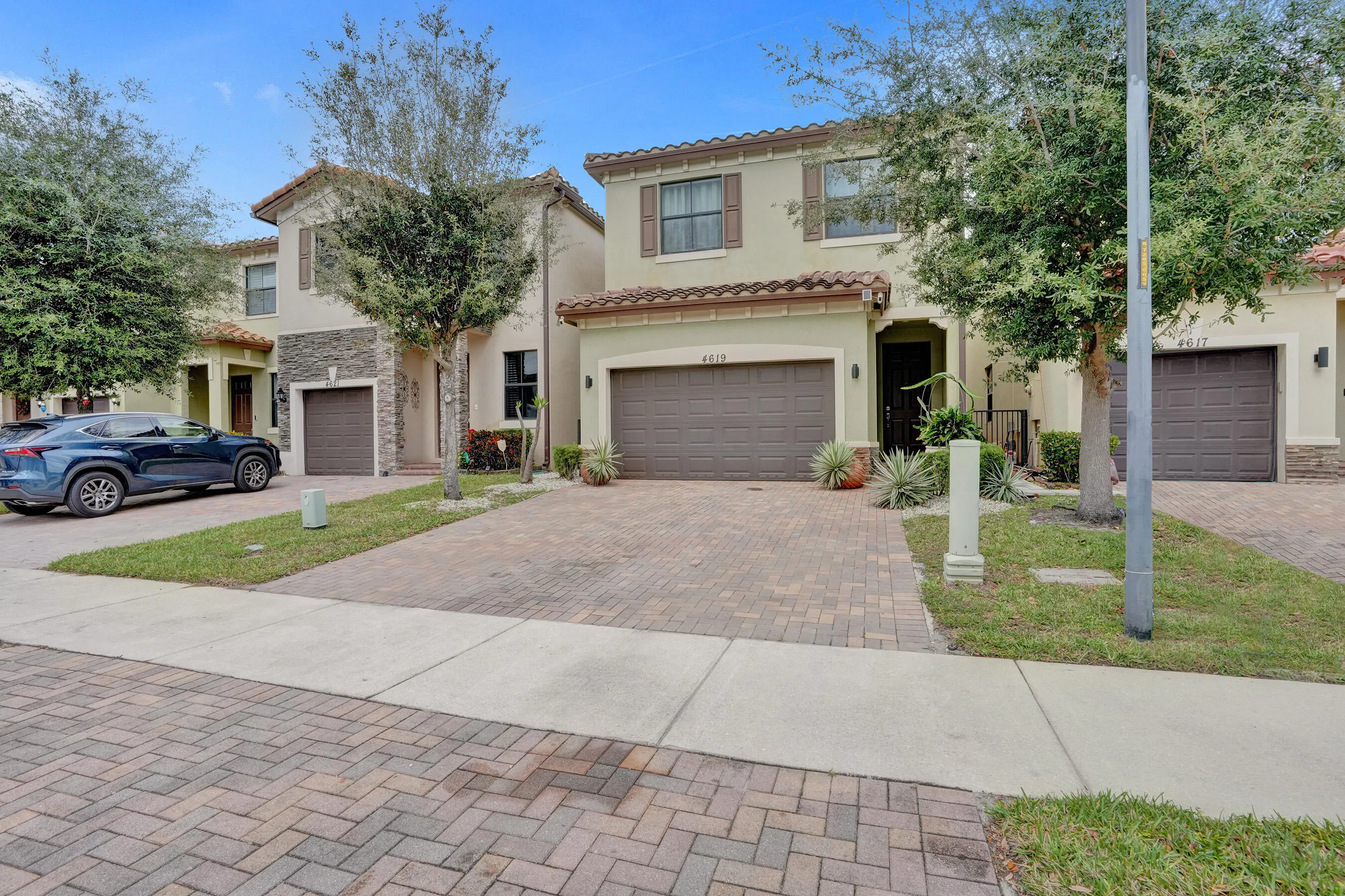 Two-story stucco exterior with tile roofing, prominent garage doors, and a paver driveway
