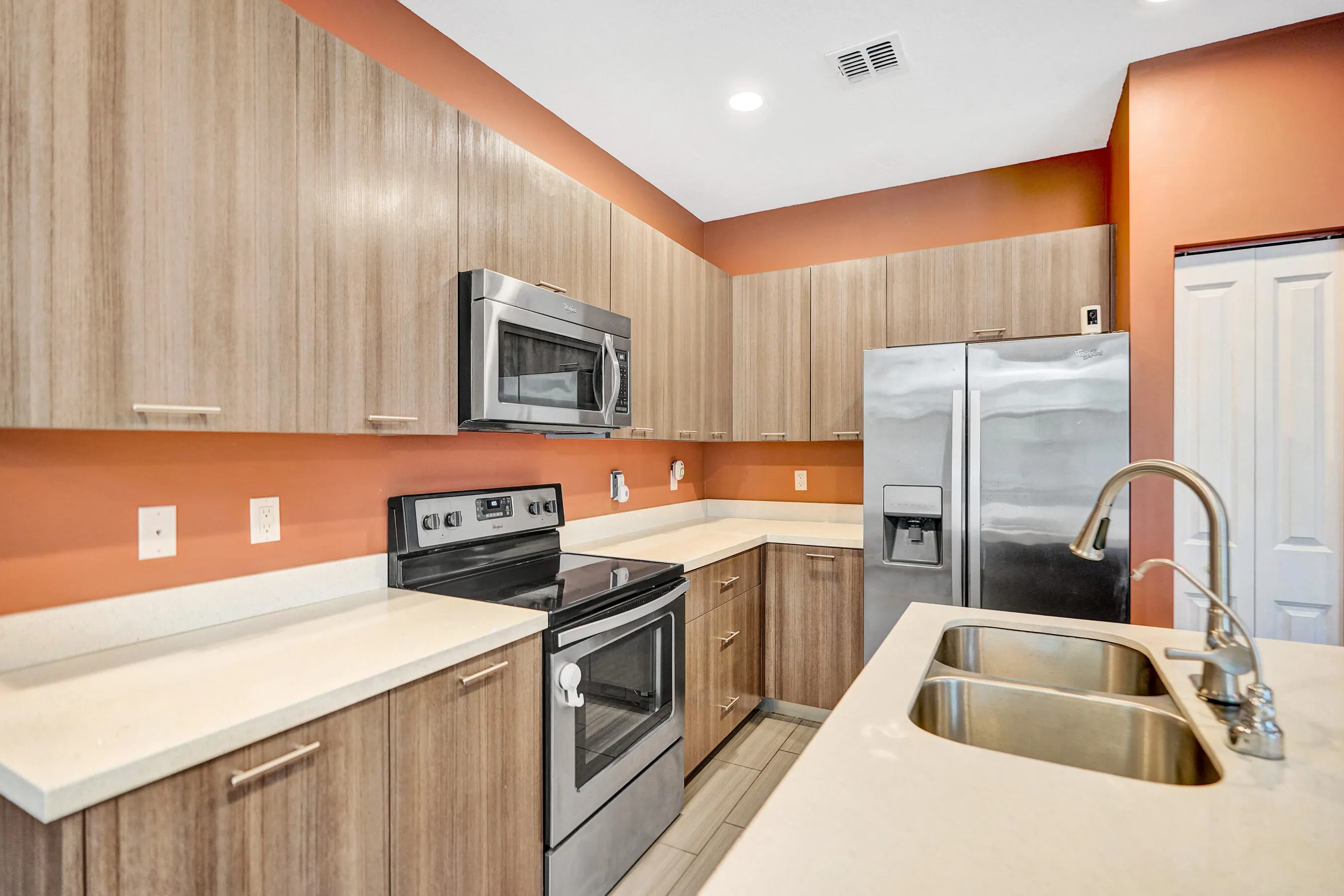 Stainless steel appliances, wood-finish cabinetry, white countertops, dual basin sink, and recessed lighting