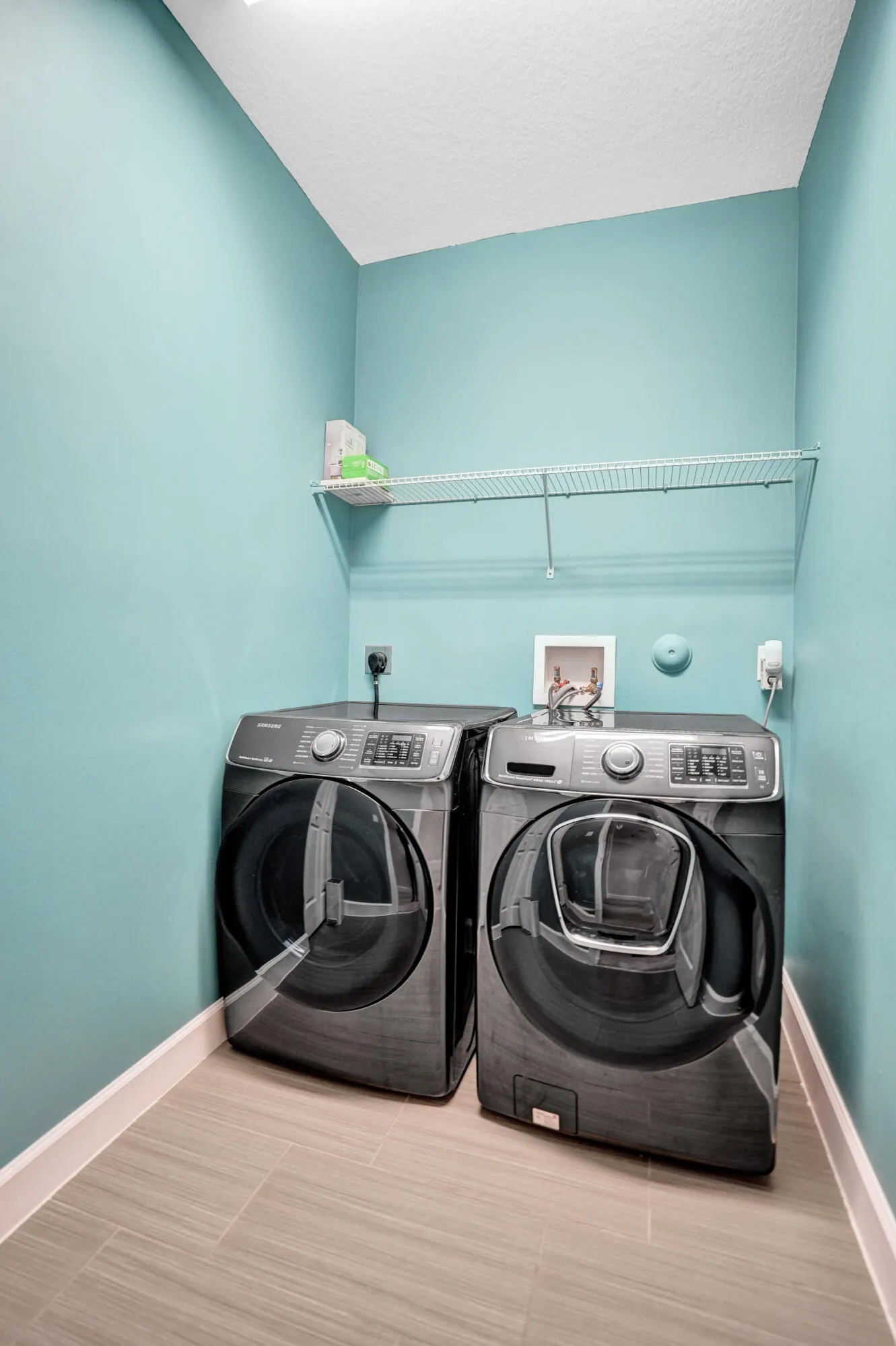 Dedicated laundry area featuring modern front-loading appliances, a built-in wire shelf, and tile flooring