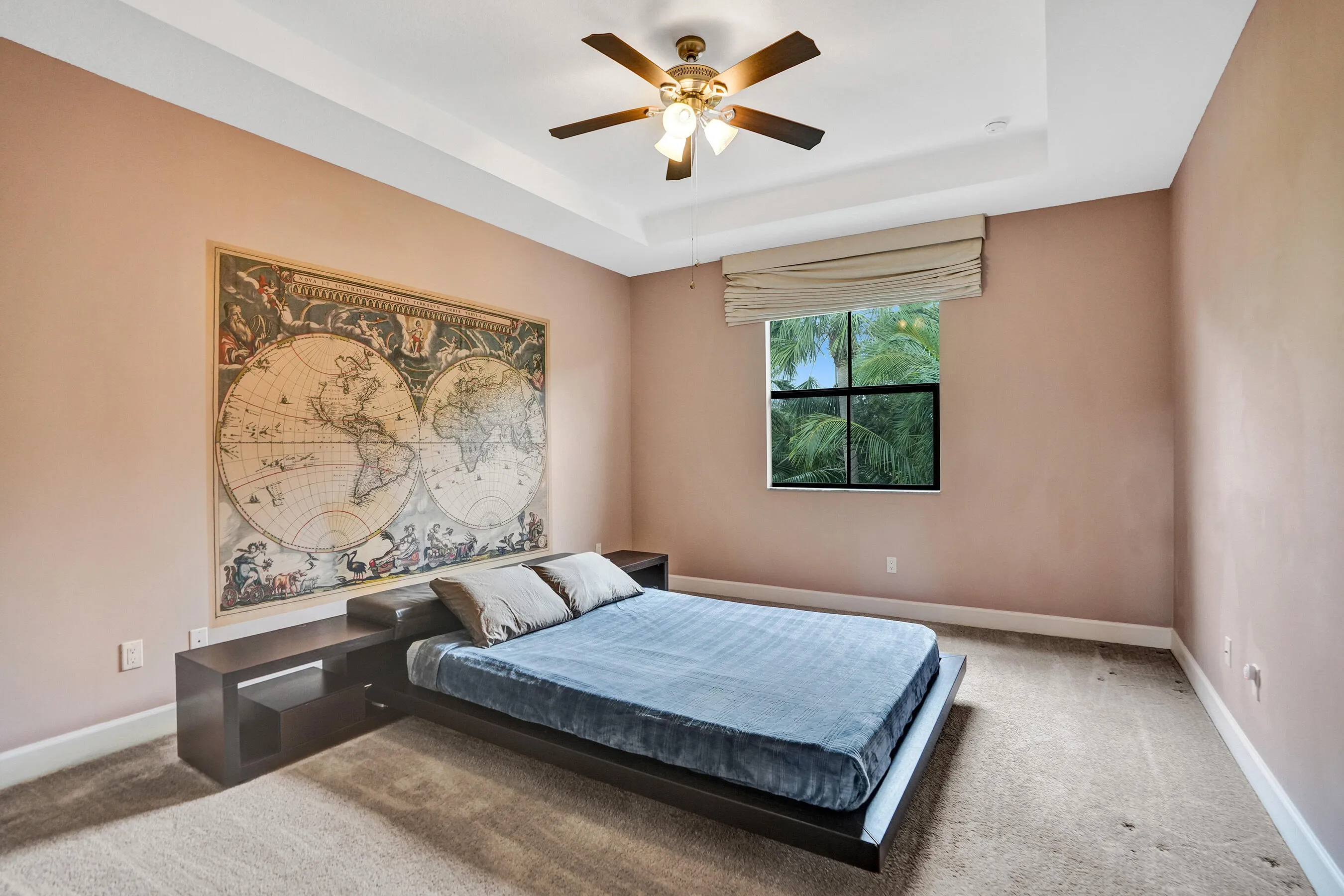 Tray ceiling with a ceiling fan light fixture, a window with a roman shade, and wall-to-wall carpeting