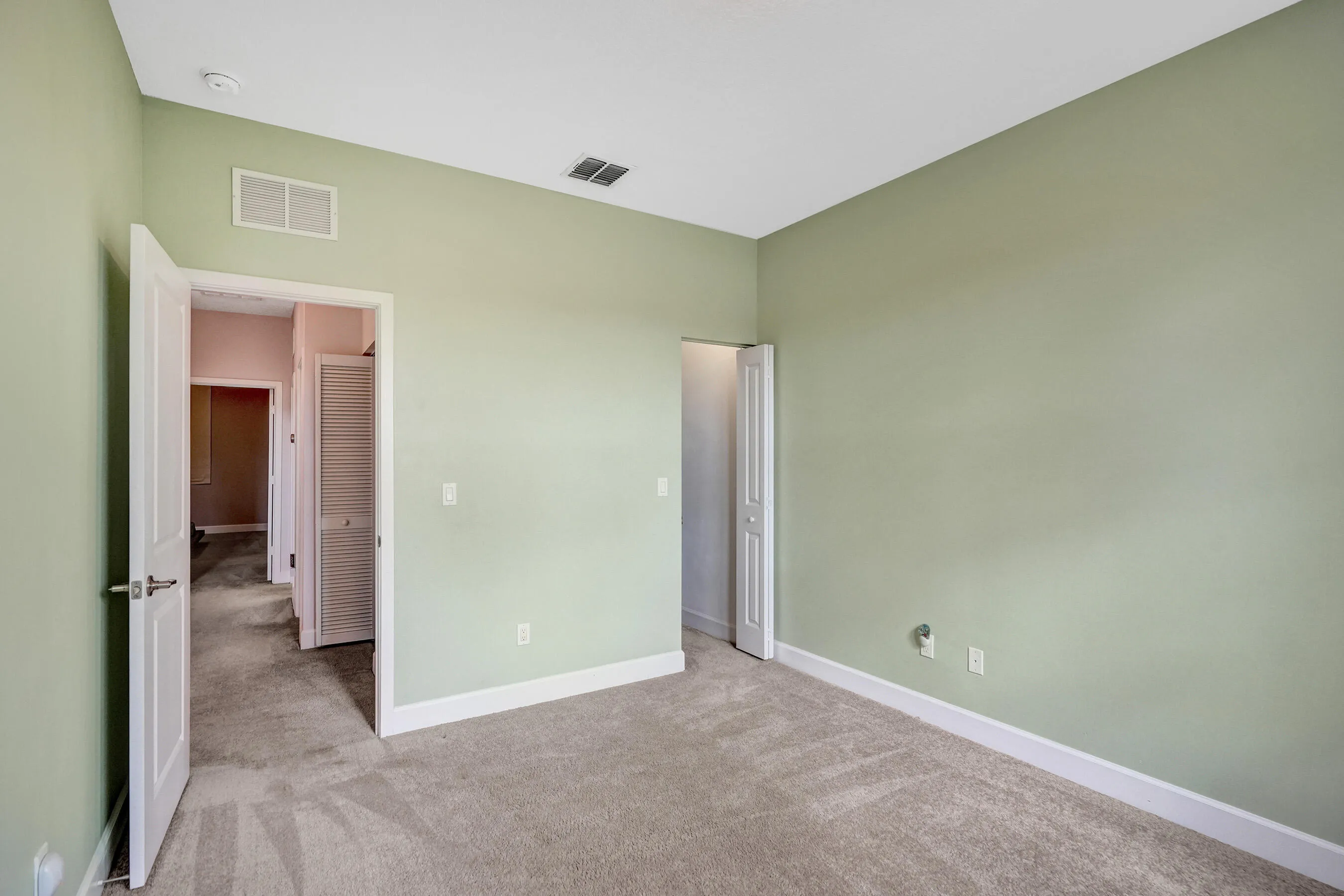 Plush carpet flooring, light green wall paint, white trim, recessed lighting, and a solid core door