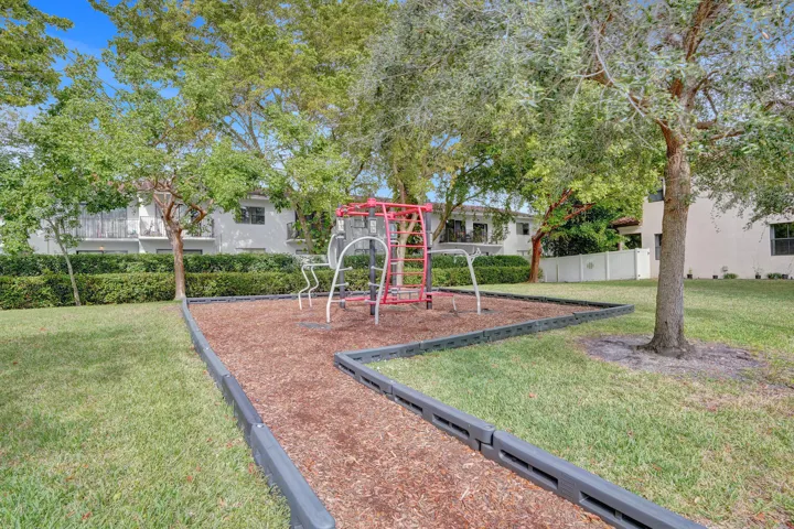 Outdoor recreation area featuring a play structure, wood chip surface, grass, trees, and perimeter curbing