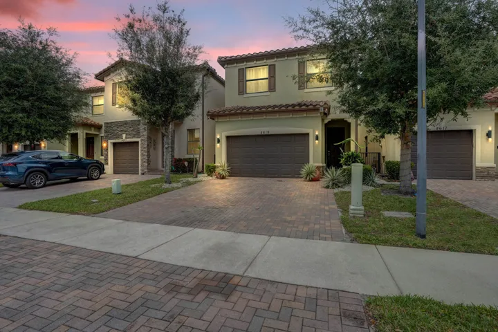 Stucco exterior with stone accents, tile roof, attached garage, and paver driveway