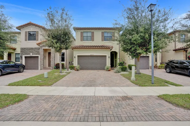 Tiled roof architecture, stucco exterior, stone accent facade, attached garage, and paver driveway