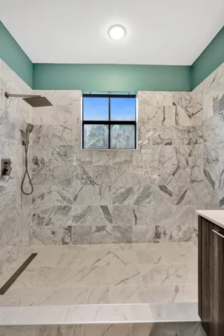 Walk-in shower with full-height marble-look tile, rainfall showerhead, linear drain, and window