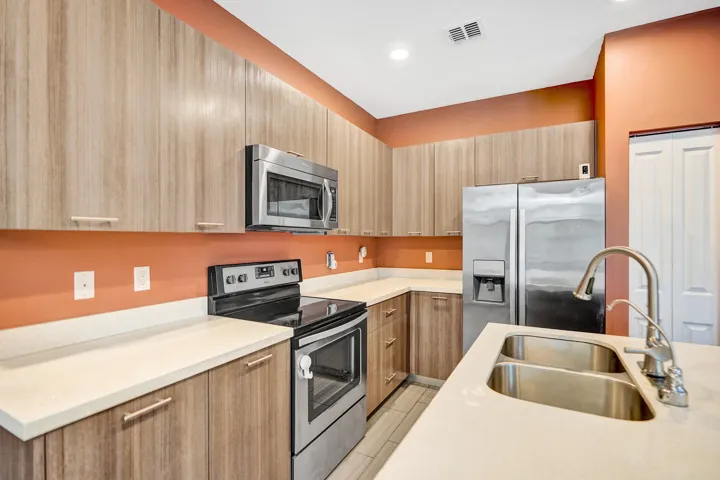 Stainless steel appliances, wood-finish cabinetry, white countertops, dual basin sink, and recessed lighting