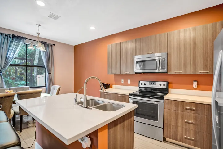 Kitchen featuring a central island with dual sinks, light-toned countertops, wood-finish cabinetry, and stainless steel appliances