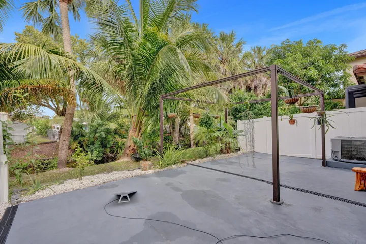 Expansive concrete patio featuring a metal pergola structure, privacy fencing, and tropical landscaping