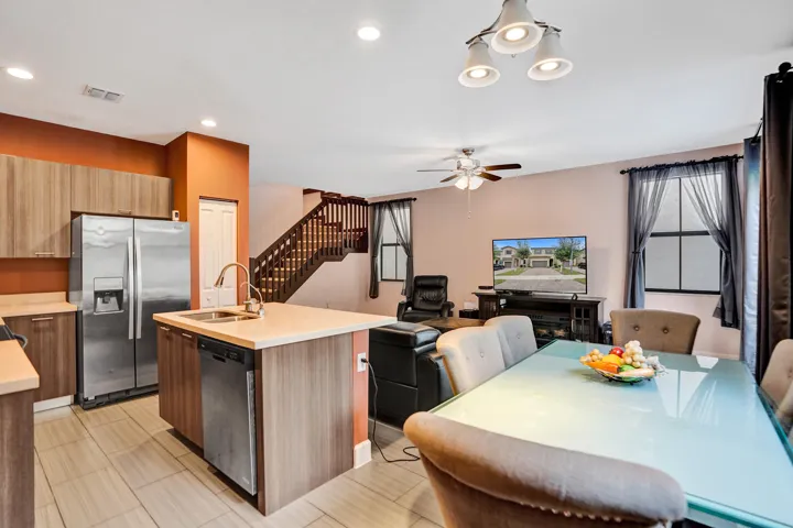 Open-concept kitchen and living area featuring a kitchen island with sink, stainless steel appliances, wood-finish cabinetry, and a ceiling fan