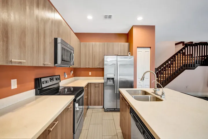 Kitchen featuring wood-finish cabinetry, stainless steel appliances, light-toned countertops, and a dual basin sink