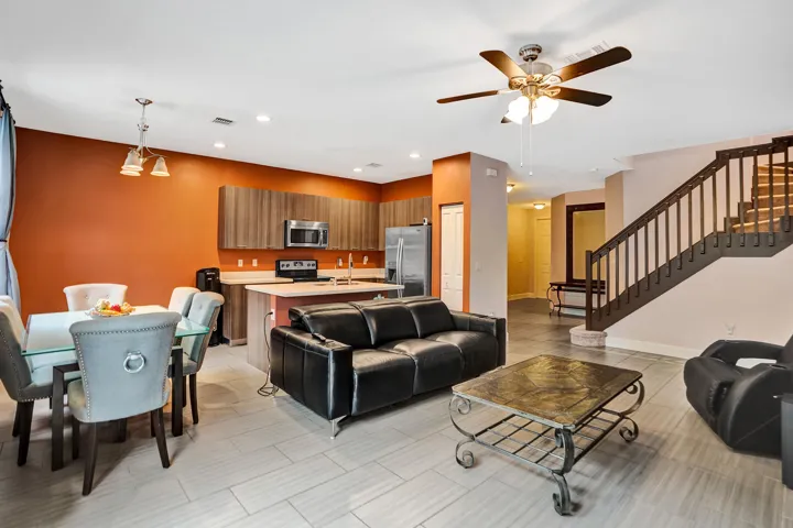 Open-concept living space with tile flooring throughout, featuring a kitchen with wood-finish cabinetry, stainless steel appliances, and a central island