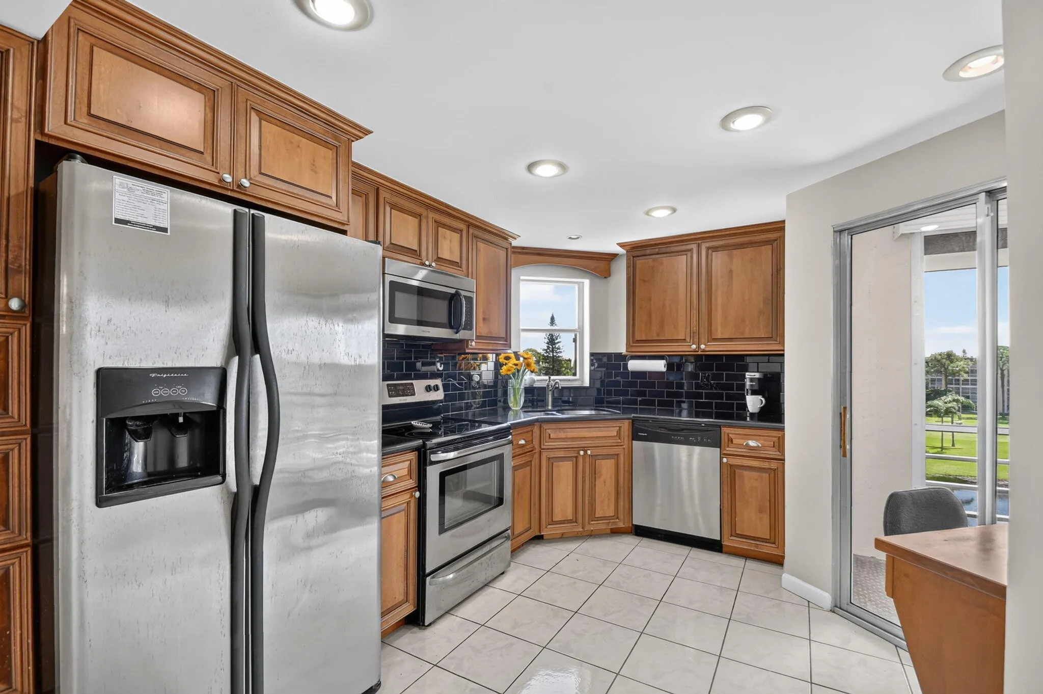 Kitchen featuring wood cabinetry, stainless steel appliances, tile flooring, recessed lighting, and a dark subway tile backsplash