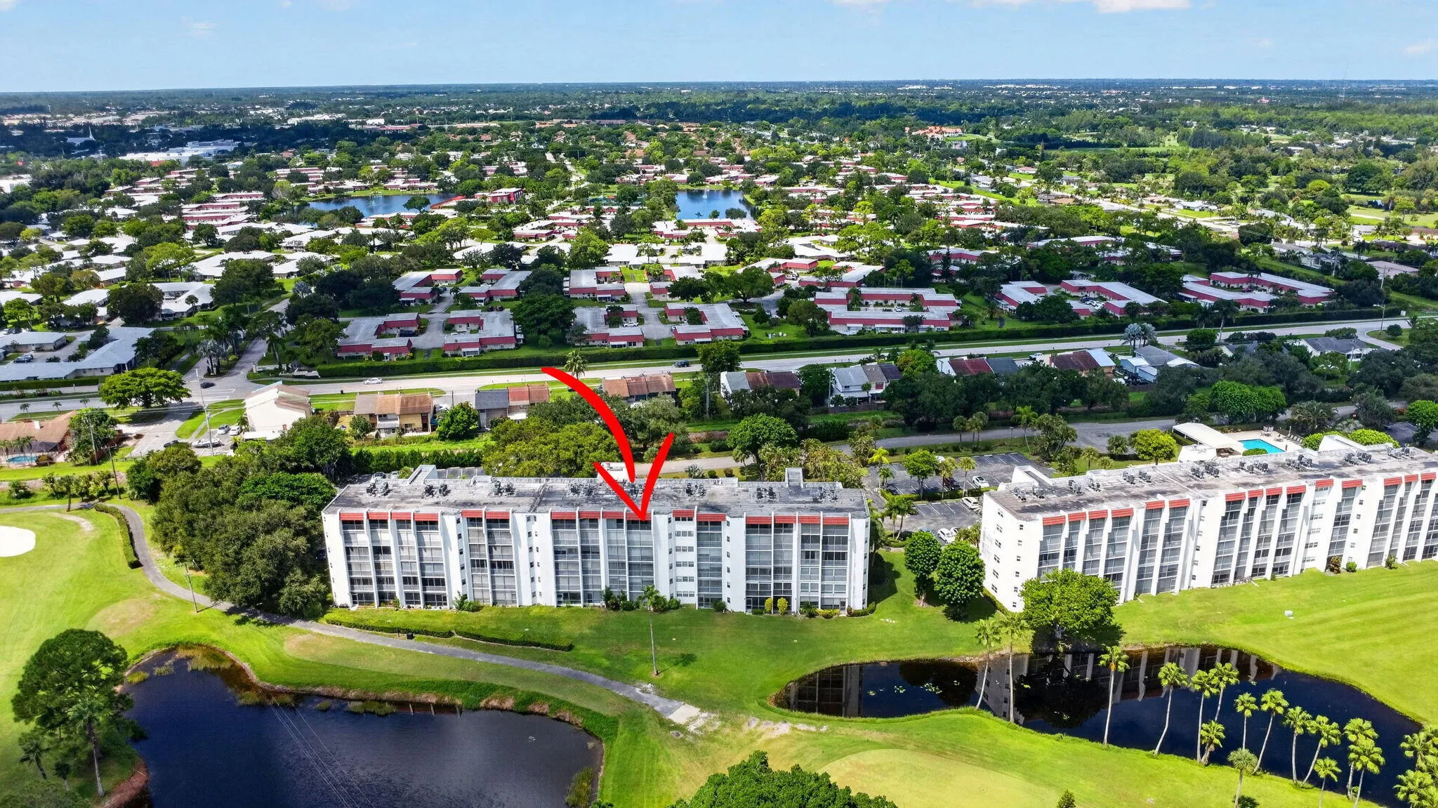 Multi-story building with multiple balconies, surrounded by mature landscaping, a golf course, and water features