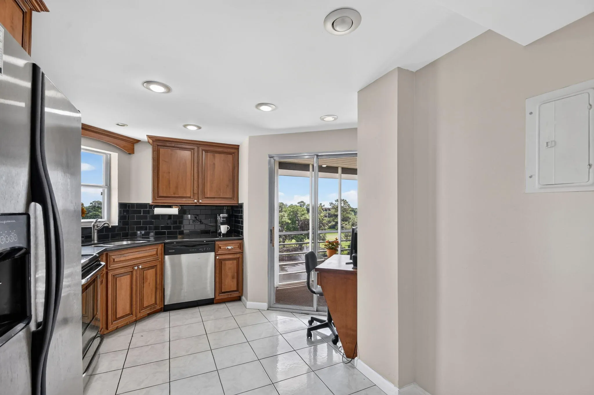 Kitchen featuring wood cabinetry, stainless steel appliances, black tile backsplash, and recessed lighting