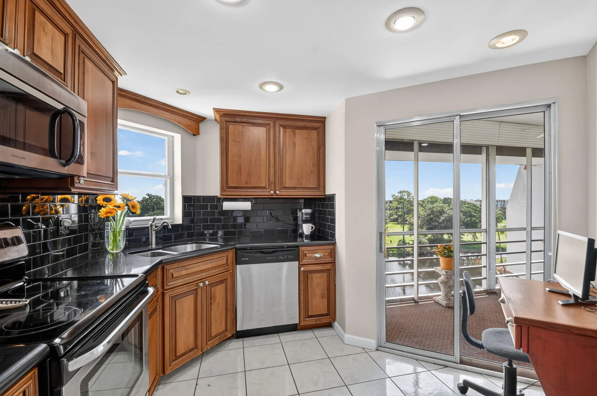 Kitchen featuring wood cabinetry, black subway tile backsplash, stainless steel appliances, and a sliding glass door to an outdoor area