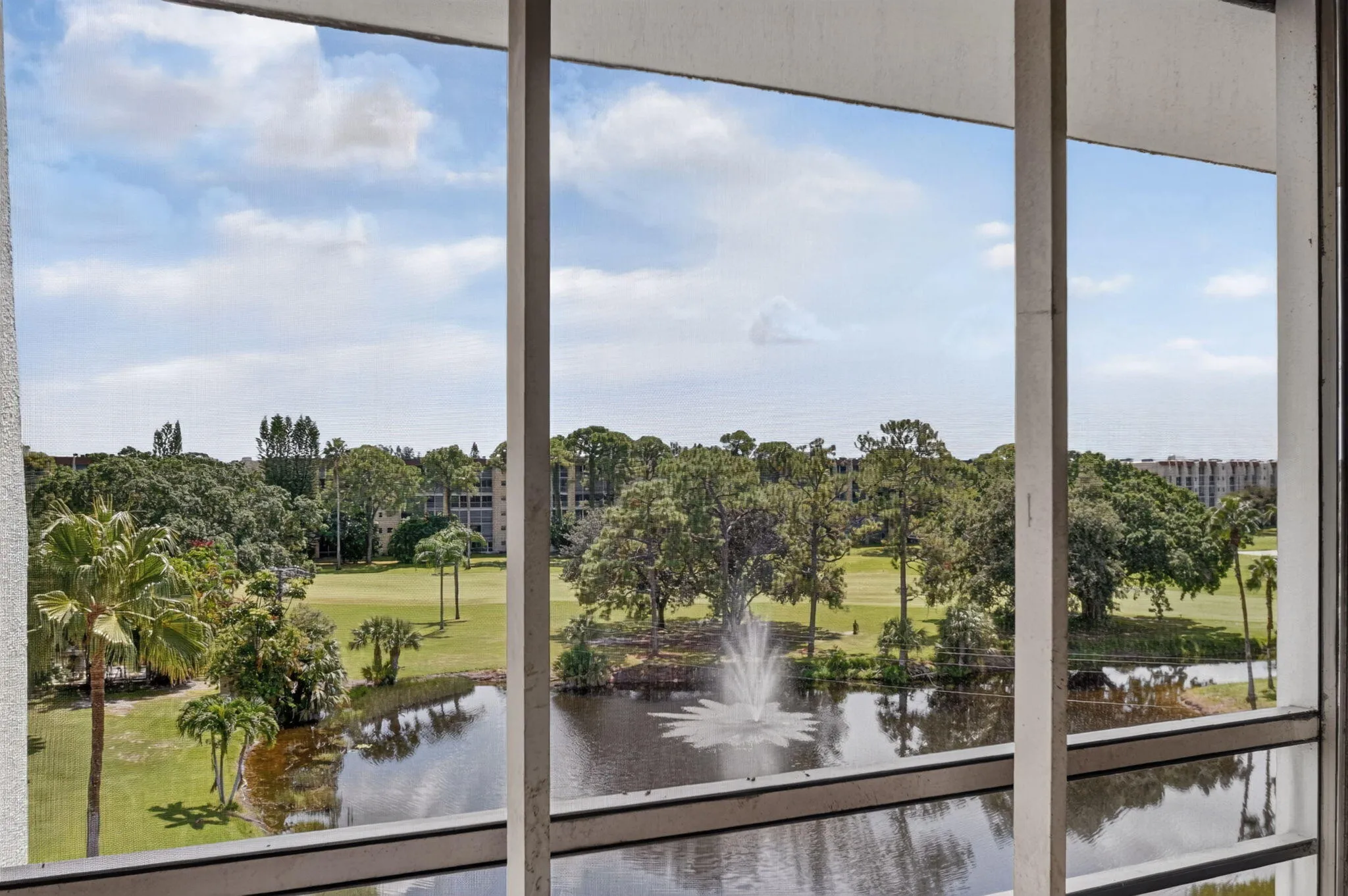 Expansive water feature with fountain, lush golf course landscaping, mature palm trees, and distant residential structures