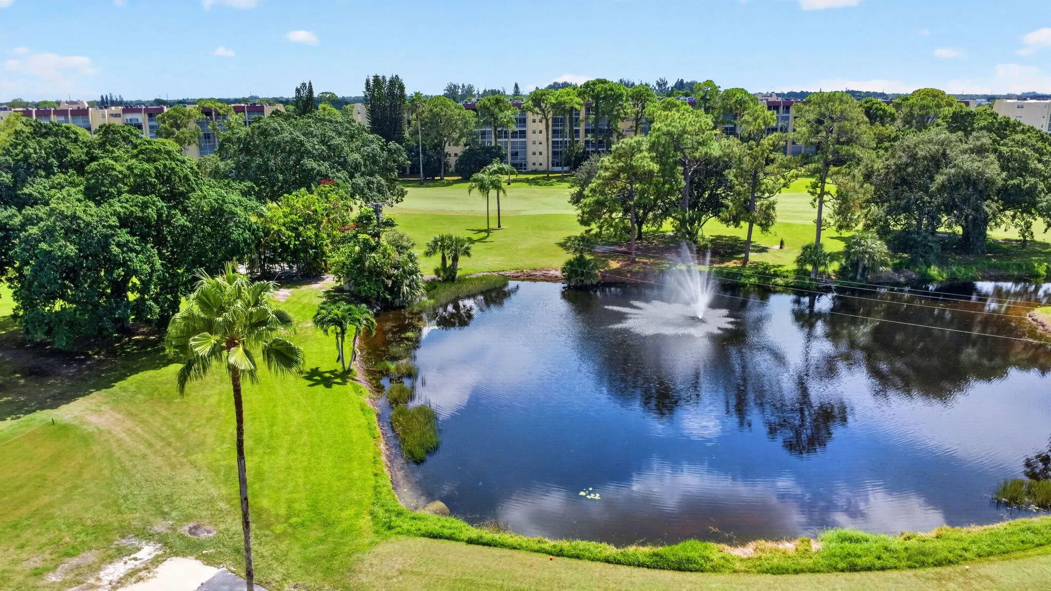 Serene lakefront grounds featuring expansive manicured lawns, mature shade trees, and a private pond with natural water features