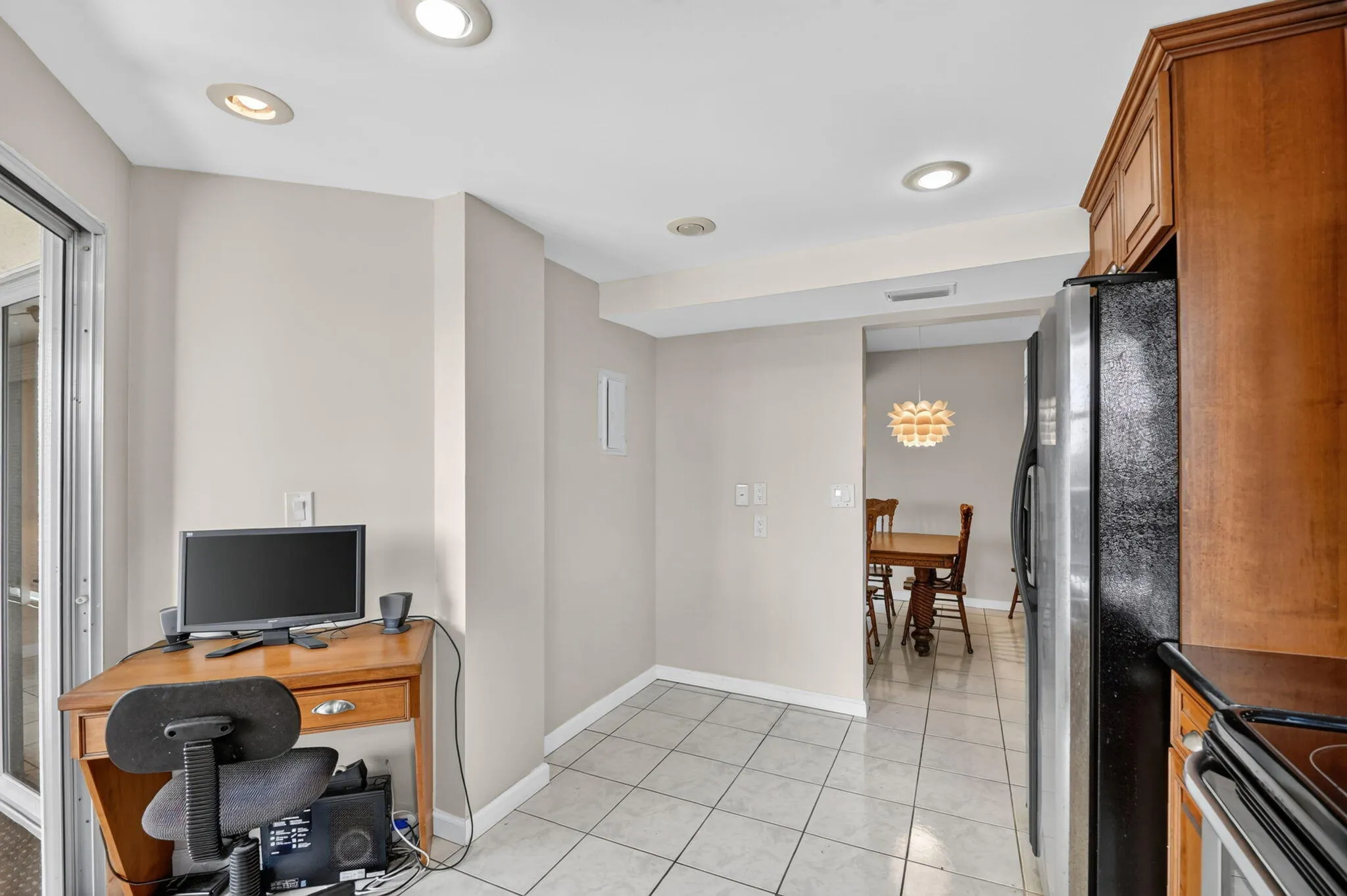 Recessed ceiling lighting, tile flooring, glass sliding door, wood-finish cabinetry, and stainless steel refrigerator