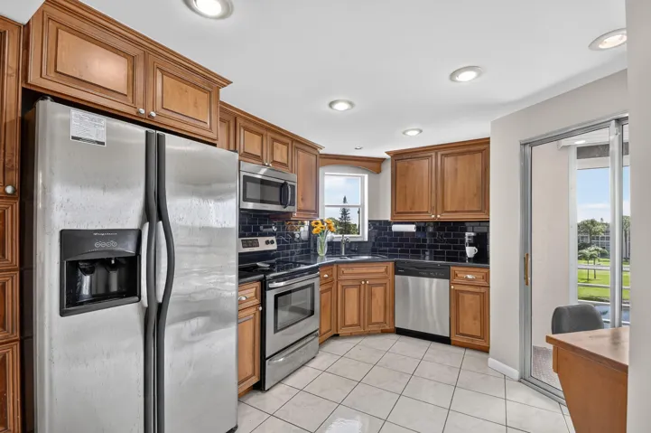 Kitchen featuring wood cabinetry, stainless steel appliances, tile flooring, recessed lighting, and a dark subway tile backsplash