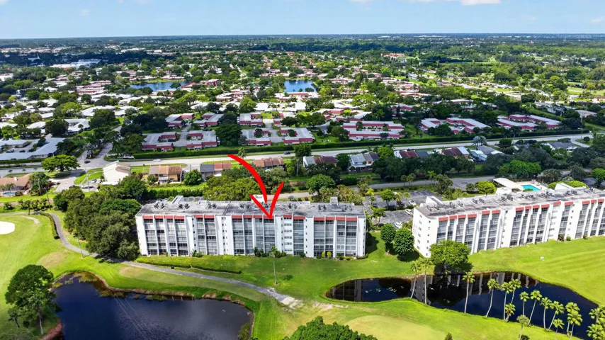 Multi-story building with multiple balconies, surrounded by mature landscaping, a golf course, and water features